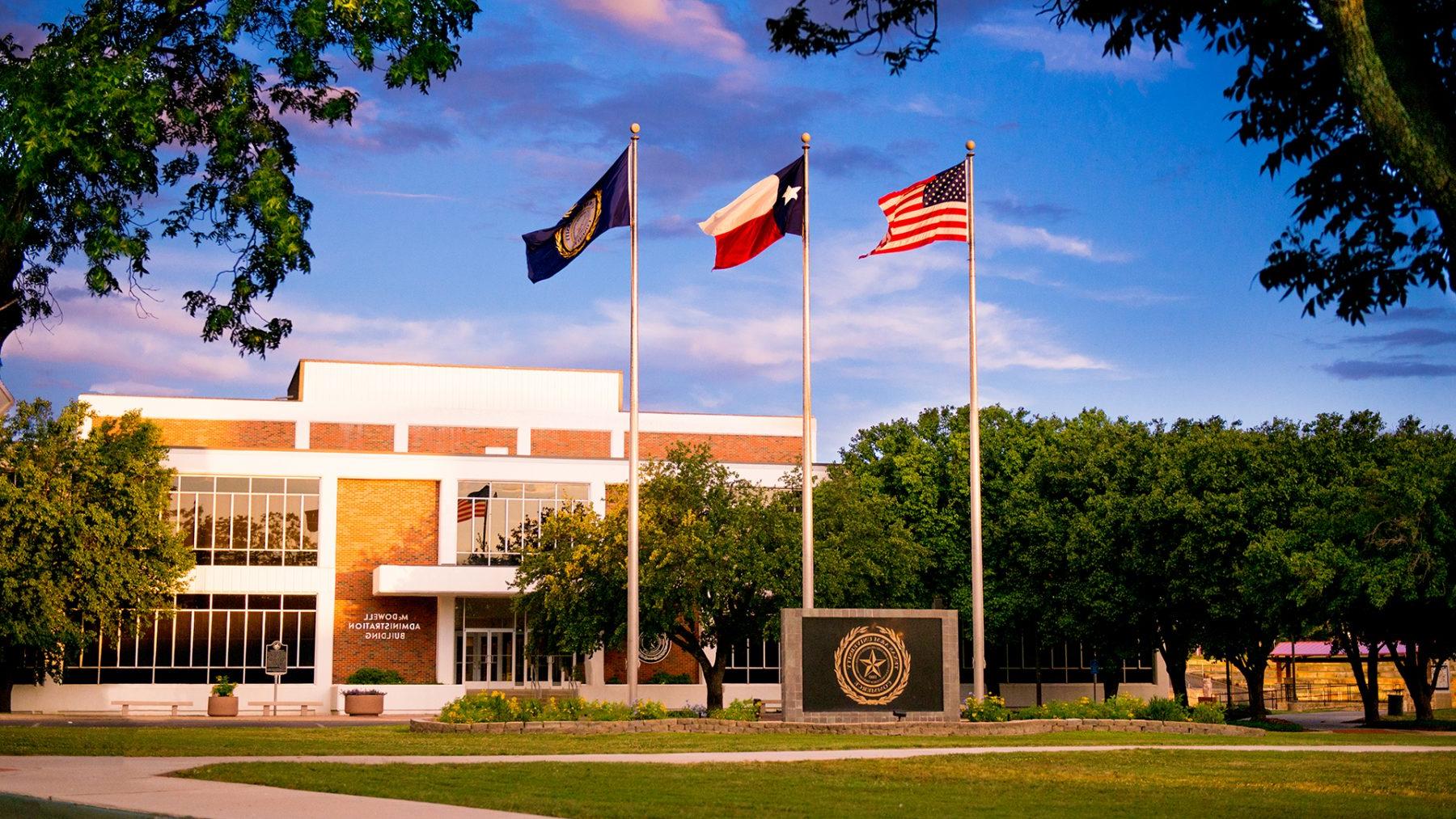 Three flag poles and the university symbol in front to the administration building on campus.